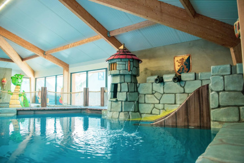 Piscina infantil interior con temática de castillo y tobogán en un parque vacacional con glamping.