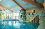 Indendørs poolområde for børn med fantasitema, rutsjebane og drage på en feriepark med glamping.