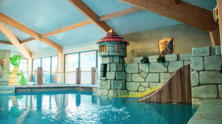 Indoor kids' pool with fantasy castle, slide, and dragon decorations at a holiday park with glamping.