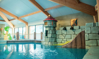 Piscina infantil interior con temática de castillo y tobogán en un parque vacacional con glamping.