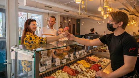 Gezin krijgt ijsje van medewerker in een moderne ijssalon van een vakantiepark met glamping.