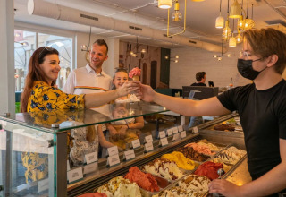 Gezin krijgt ijsjes van medewerker in een moderne ijssalon op een glamping vakantiepark.