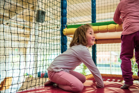 Dos niños juegan felices en una zona de juegos interior con redes en un parque vacacional con glamping.