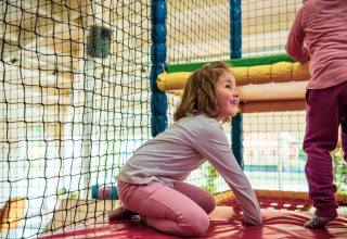 Zwei Kinder spielen lachend in einem Indoor-Spielbereich eines Ferienparks mit Glamping-Unterkünften.