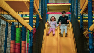 Two children laughing as they slide down a yellow slide in an indoor play area at a glamping holiday park.