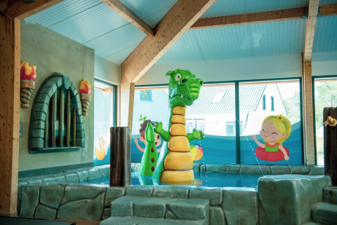 Innenbereich eines Ferienparks mit Drachen-Wasserfontäne und bunten kinderfreundlichen Dekorationen.
