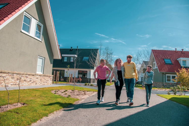 Family walking on a path between modern holiday park homes on a sunny day with clear blue sky.