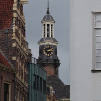 Urban scene with historic clock tower centered among narrow streets and old brick buildings under grey sky.