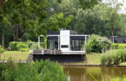 Moderna cabina glamping sul lago in un parco vacanze, circondata da verde lussureggiante e alberi alti.
