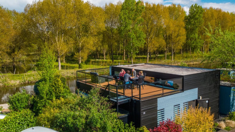 Des vacanciers sur la terrasse d’un hébergement glamping moderne, entouré d’arbres, dans un parc de vacances.