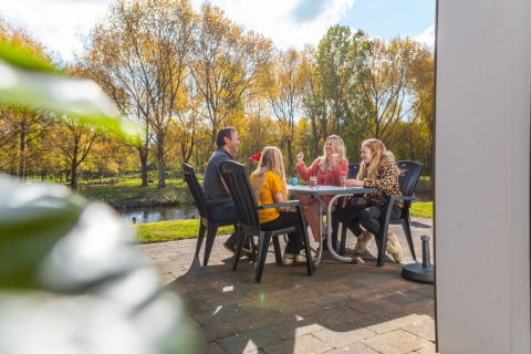 Gezin geniet buiten van een maaltijd in een vakantiepark met glamping, omringd door bomen.
