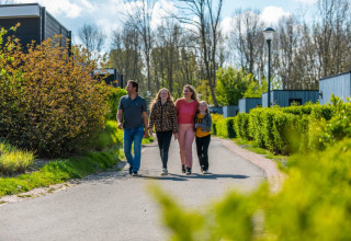 Family walking on a path at a holiday park surrounded by greenery and glamping cabins on a sunny day.
