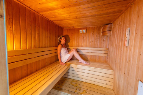 Vrouw rust uit in een houten sauna op een vakantiepark met glampingverblijven.