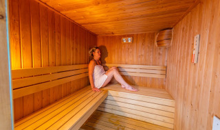 Mujer relajándose en una sauna de madera en un parque vacacional con opciones de glamping.