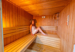 Vrouw rust uit in een houten sauna op een vakantiepark met glampingverblijven.