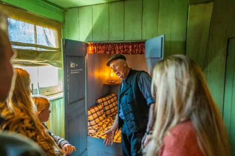 Ein Führer erklärt einer Gruppe eine historische Schlafkabine in einem Glamping-Ferienpark.