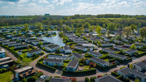 Vista aérea de un parque vacacional con alojamientos glamping modernos, zonas verdes y un lago central.