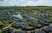Luftfoto af et feriepark med moderne glamping-hytter, grønne områder og en sø omgivet af træer.