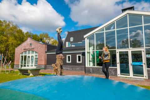 Kids are playing on a large outdoor bouncy cushion in front of glamping accommodations at a holiday park.