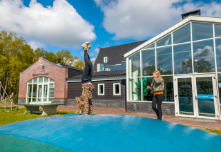 Børn leger på en stor udendørs pude foran glampingindkvarteringer i et feriepark med blå himmel.
