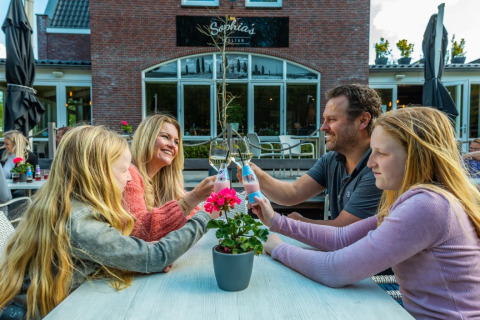Una familia brinda junta al aire libre en una mesa de un parque vacacional con opciones de glamping.