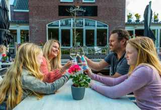 En familie sidder sammen udendørs ved et bord og skåler på en glampingferie i en ferielandsby.