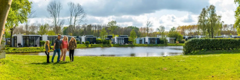 Family enjoying time by a lake at a holiday park with modern glamping lodges and lush green surroundings.