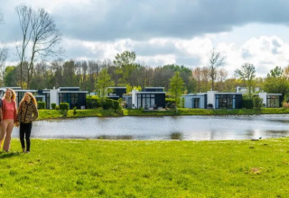 Familie nyder udsigten ved en sø i et feriepark med moderne glampinghytter omgivet af natur.