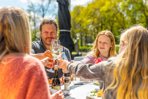 Gezin geniet samen van eten en toast op een zonovergoten dag op een glamping vakantiepark.