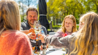 Familia brindando al aire libre mientras disfruta de una comida soleada en un parque de glamping.