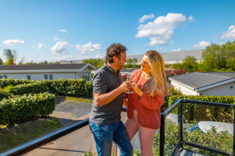 Pareja disfrutando de bebidas en la terraza de un parque vacacional con alojamientos glamping y sol.