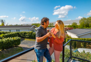 Paar genießt Getränke auf der Terrasse in einem Ferienpark mit Glamping, umgeben von Natur.