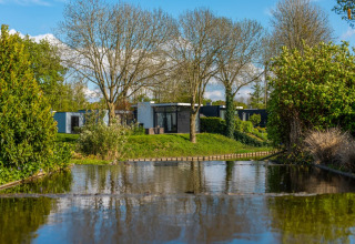 Moderne glampinghuizen aan een vijver, omgeven door bomen en groen in een vakantiepark.