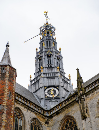 Torre de iglesia con reloj y detalles dorados en un día nublado, desde un parque vacacional con glamping.