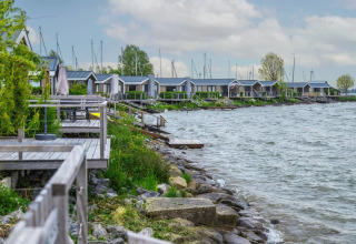 Træhytter ved søbred i feriepark, glamping indkvartering med bådebroer og frodig natur, idyllisk udsigt.