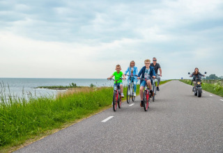 Familie cykler og kører scooter langs kystvejen nær et feriepark med glampingmuligheder.