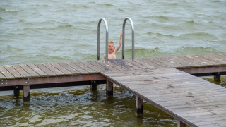 Child climbing a swim ladder attached to a wooden pier over a lake at a holiday park with glamping.