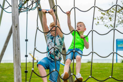 Dos niños juegan en una red de cuerdas en el parque de una zona de glamping en un parque vacacional.