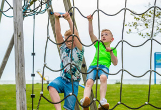 Dos niños juegan en una red de cuerdas en el parque de una zona de glamping en un parque vacacional.