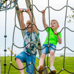 Two boys climbing on a rope net at a playground in a holiday park offering glamping accommodations.