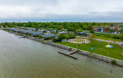 Vista aérea de un parque vacacional con alojamientos glamping junto al agua, áreas verdes y parque infantil.