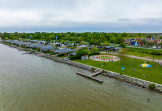 Luchtfoto van een vakantiepark met glampingaccommodaties aan het water, groene zones en speeltuin.