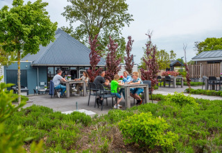Udendørs spiseområde på en feriepark med glamping, familier nyder måltider omgivet af grønne planter.