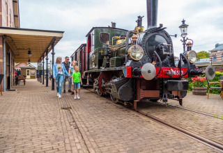 Familie går forbi et damptog på en charmerende station i en feriepark med glamping i Holland.
