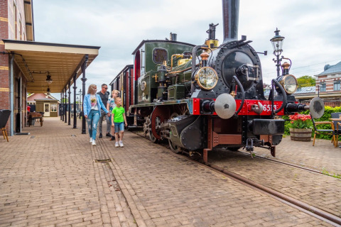 Familie går forbi et damptog på en charmerende station i en feriepark med glamping i Holland.