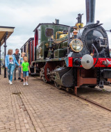 Family walking past a historic steam train at a vintage station in a glamping holiday park in the Netherlands.