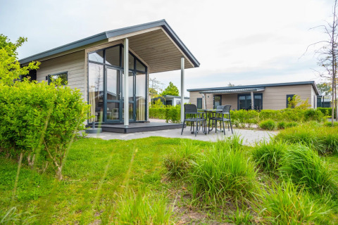 Photo of a holiday park with modern glamping lodges, outdoor terrace, and green landscaping in daylight.