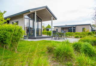 Photo of a holiday park with modern glamping lodges, outdoor terrace, and green landscaping in daylight.