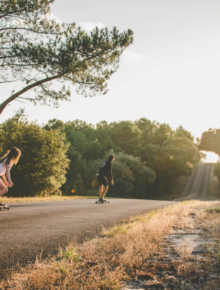 Two people skateboarding on a forest road at sunset near a holiday park offering glamping accommodations.