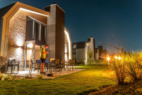 Cabaña moderna de glamping en un parque vacacional, iluminada de noche con persona en la terraza.